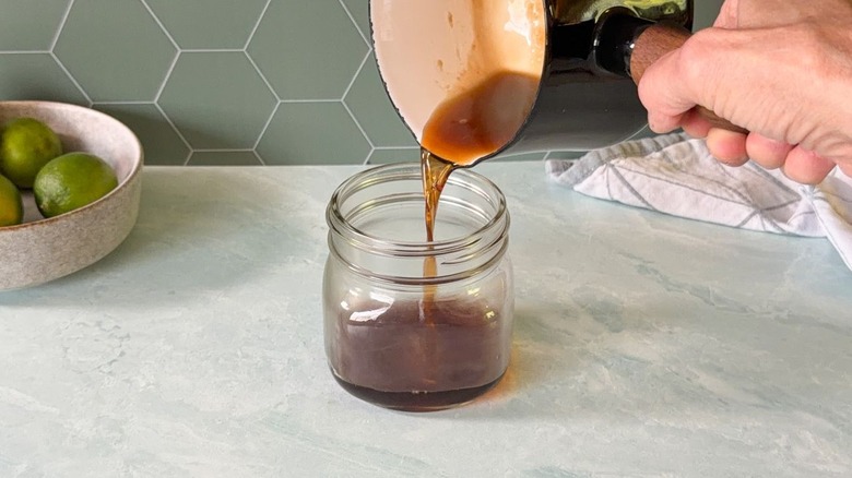 Pouring hot turbinado sugar syrup into glass jar from saucepan