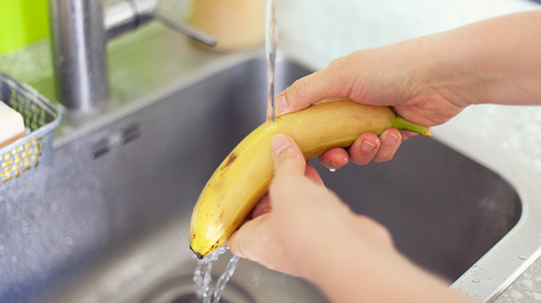 Person washing banana in a sink. Close up.