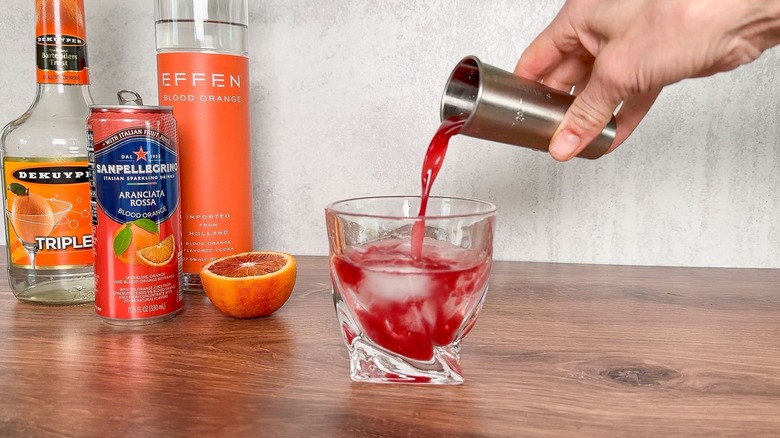 Pouring fresh blood orange juice over ice in rocks glass