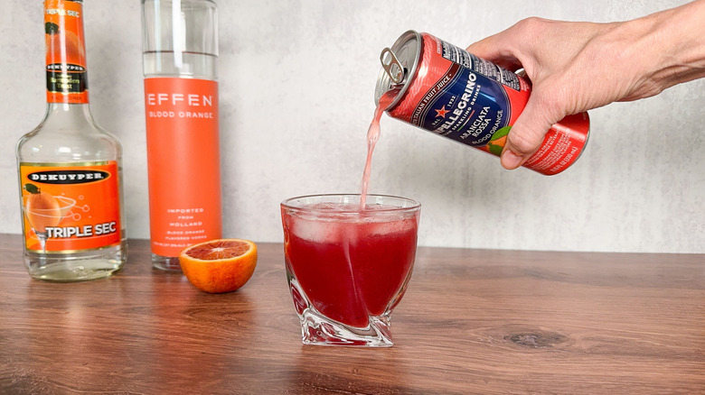 Pouring blood orange soda into fruity and fun blood orange crush cocktail