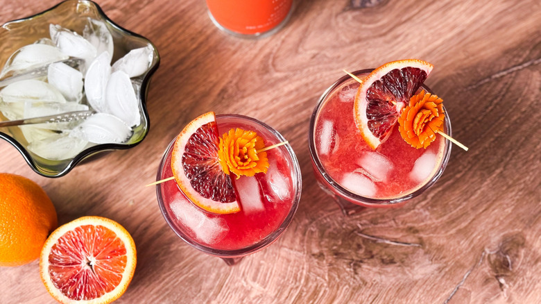 Fruity and fun blood orange crush cocktails on table with bowl of ice and blood oranges