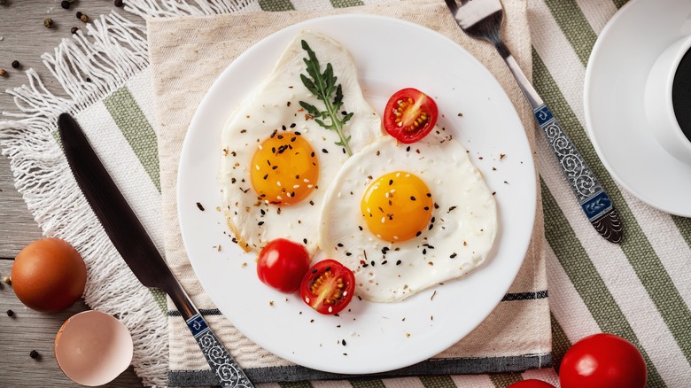 Table setting with fried eggs, tomatoes, and garnish on a white plate.