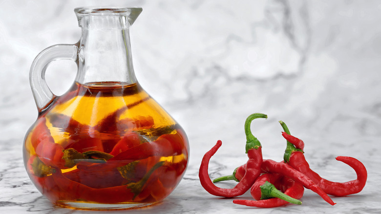 A bottle of chili oil beside a pile of red chilis.