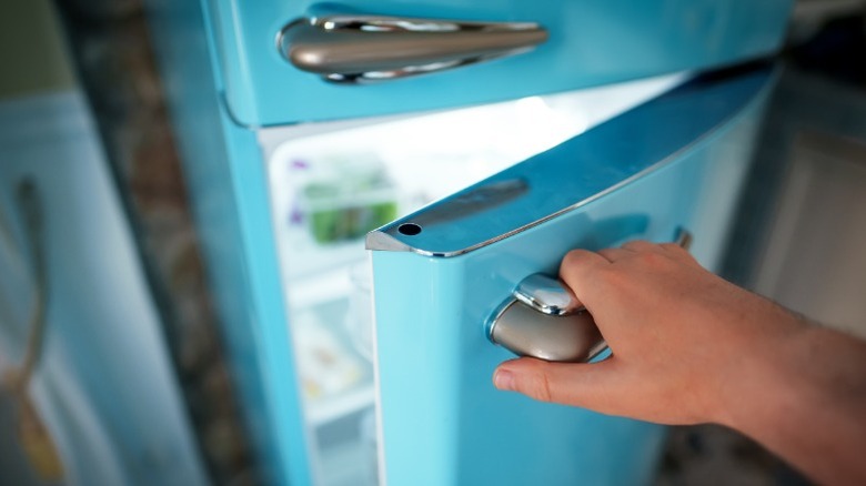 A hand opening the door of retro-style refrigerator with bright light shining within.