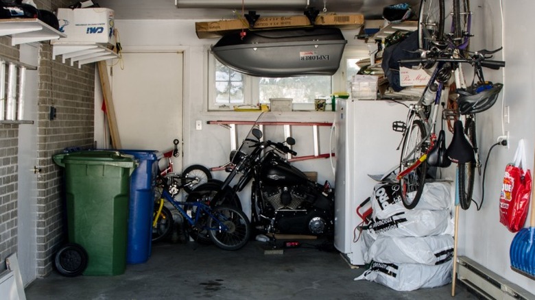 A refrigferator in a garage surrounded by outdoor items.