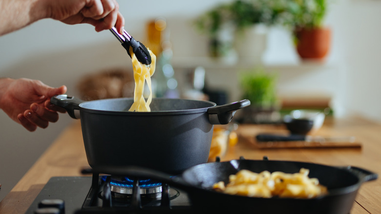 man boiling pasta noodles on a gas stove