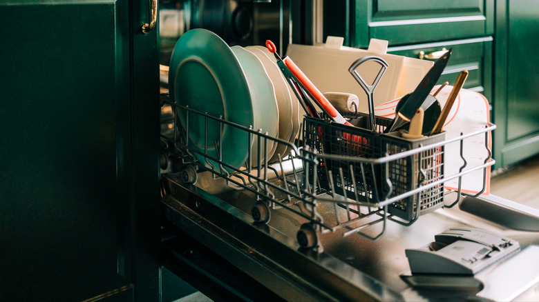 Open dishwasher bottom rack with dishes in dark green kitchen