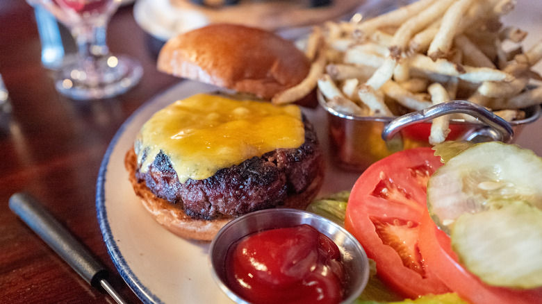 A cheeseburger on a plate with an array of toppings and an order of french fries.