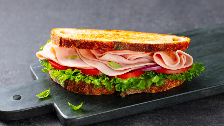 Ham sandwich with lettuce and tomato on black cutting board