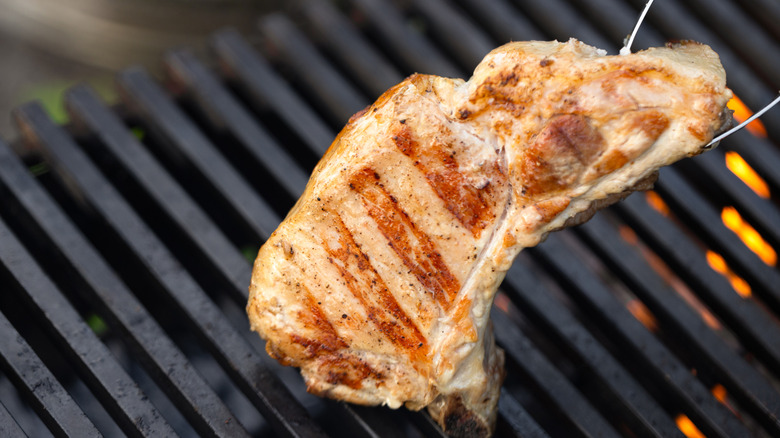 Person grilling a pork chop flipps it with tongs