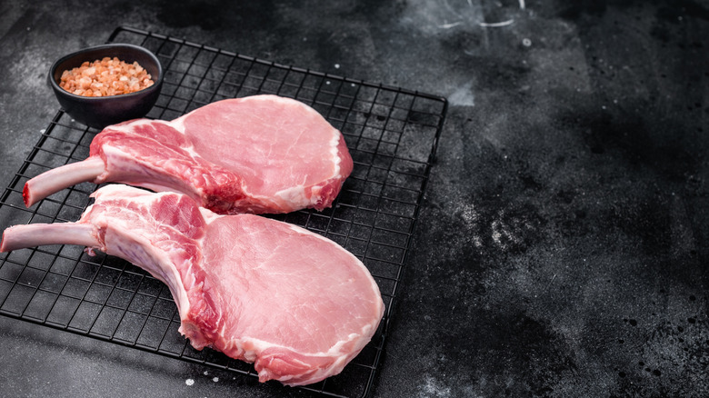 Bone-in pork chops on a black wire rack with seasoning in a bowl