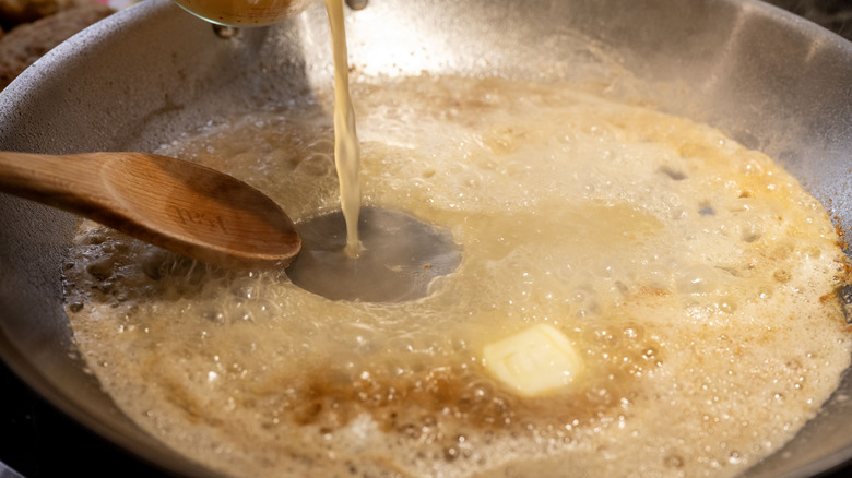 Person making a pan sauce with butter, broth, and a wooden spoon