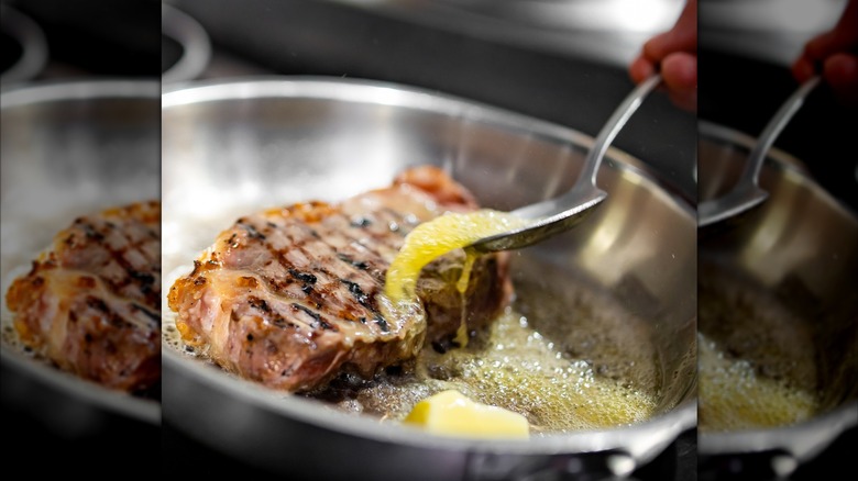 Person butter-basting a pork chop in a pan