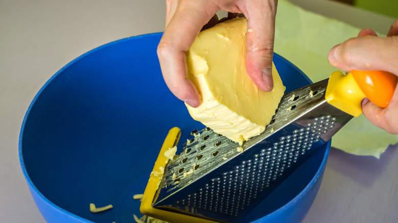 Grating frozen butter into wheat flour on wooden board.