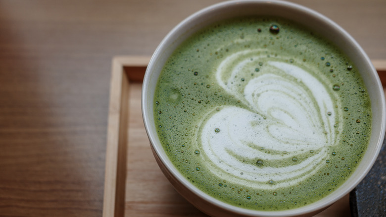 Matcha latte with heart latte art on a wooden plate