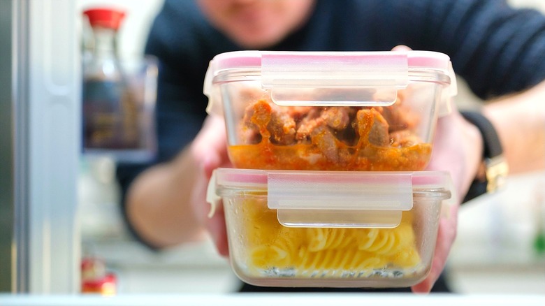 Person holding two resealable glass food containers with leftovers and cooked noodles
