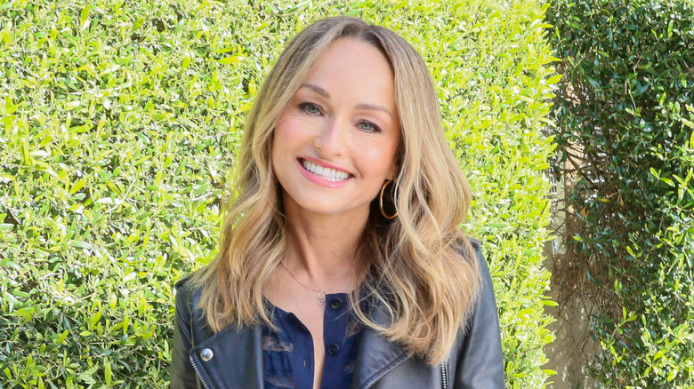 Giada De Laurentiis wearing leather jacket and blue shirt posing against hedges