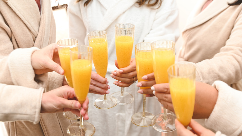 Hands clinking mimosa glasses together