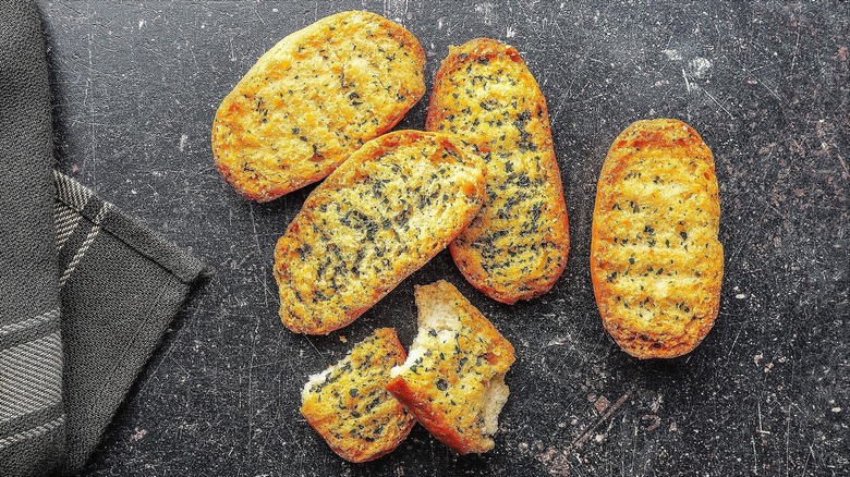 Pieces of toasted, herb-infused garlic bread on a black surface with white speckles
