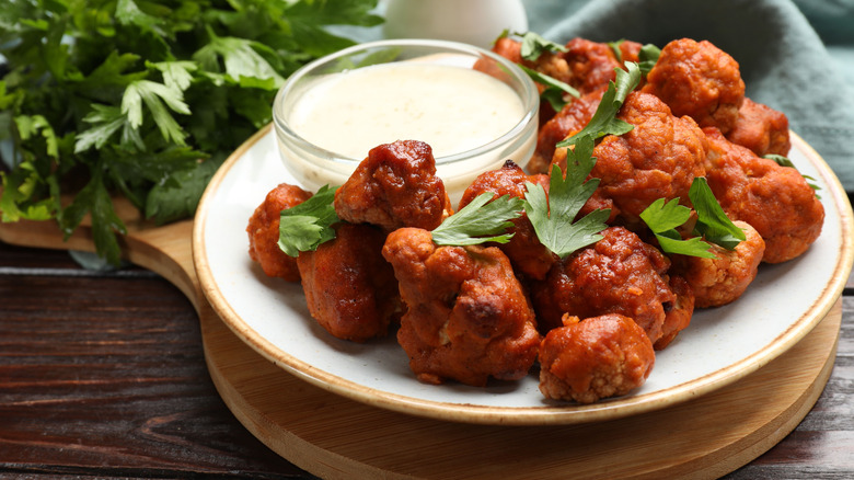 Baked cauliflower buffalo wings with parsley and sauce on wooden table.