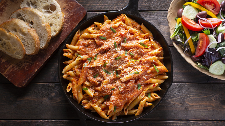 A flat lay of a gorgeous dinner spread with pasta right in the center, fresh salad on the right, and slices of rustic bread on the left.