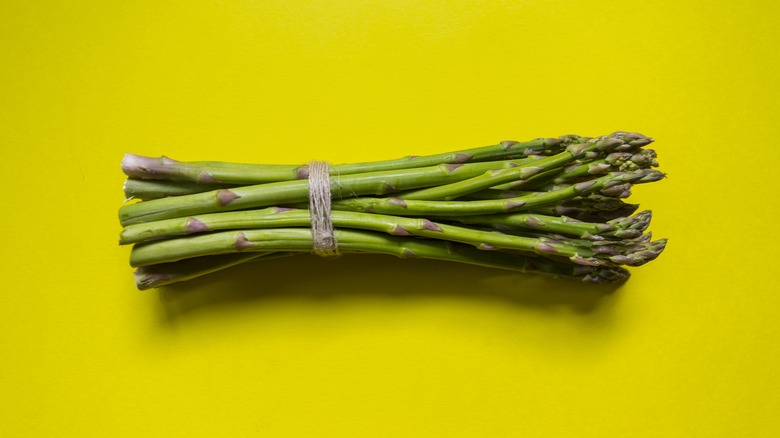 A bundle of fresh asparagus on a yellow background.
