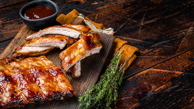 Glazed baby back ribs on a wooden board with sauce and herbs on the side