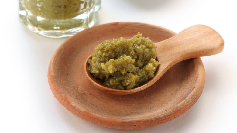A dollop of yuzu kosho Japanese paste on a wooden spoon sitting on a matching saucer next to a jar of the stuff.
