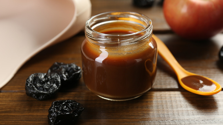 a small bottle of prune baby food beside whole prunes on a table