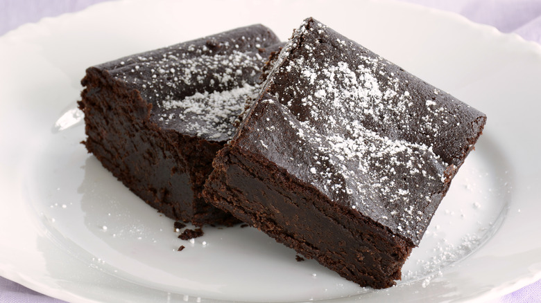 two fudgy brownies sprinkled with icing sugar on a white plate