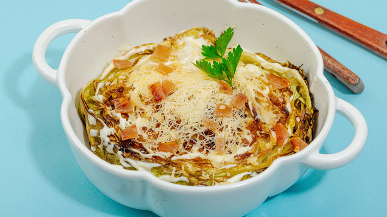 A cabbage steak in a bowl topped with cheese, bacon, and white sauce