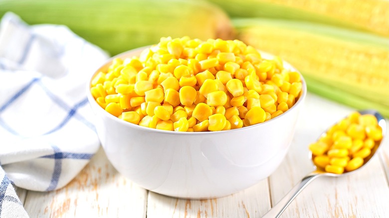 White bowl full of canned yellow corn on a white-washed wooden table