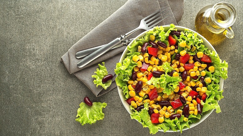 Green salad with black beans, chopped red bell peppers, and canned corn in a white bowl on a grey surface
