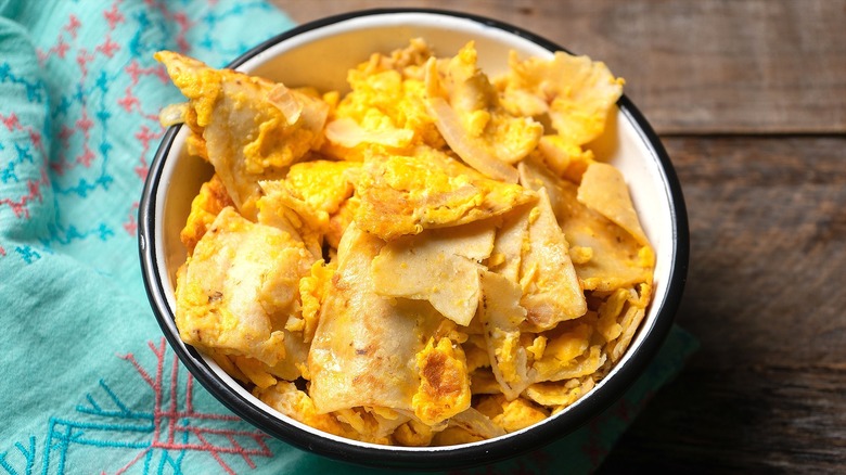 Migas or scrambled eggs, broken tortillas, and cheese in a white bowl with black trim.
