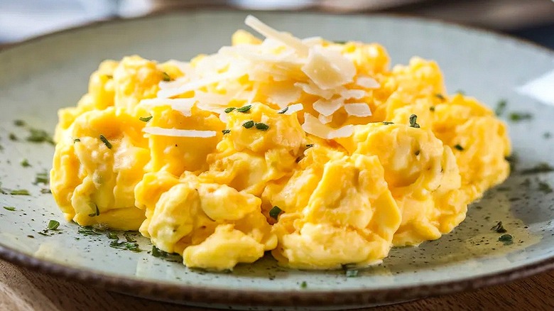 Close-up of scrambled eggs with white shredded cheese and green herbs on a speckled ceramic plate
