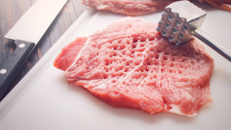 Raw meat with tenderizing mallet on a white cutting board