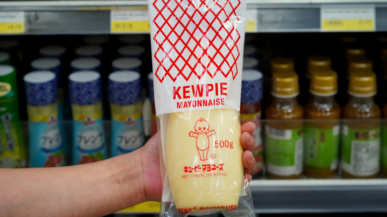 Close up of Japanese style Kewpie brand mayonnaise held in hand in a local supermarket aisle with product labels visible in the background.