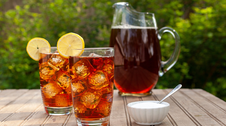 Two glasses of iced sweet tea with a pitcher of tea and a bowl of sugar.