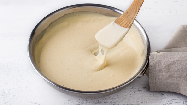 A spatula dragged through a bowl of cheese sauce against a countertop
