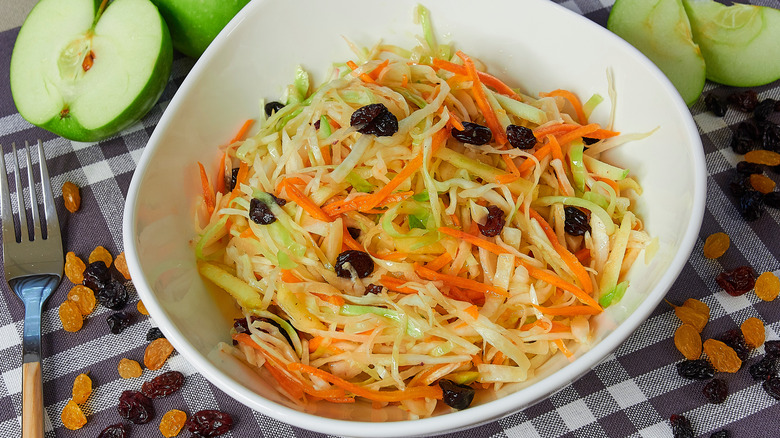 Coleslaw in a white bowl with dark raisins