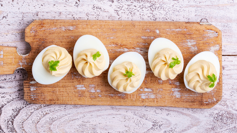 A row of deviled eggs with herb garnish on a wooden cutting board