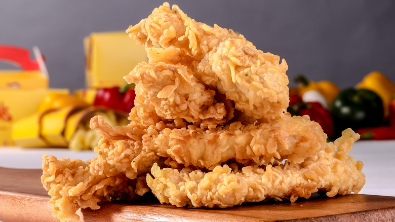 PIle of crispy chicken tenders on a wooden cutting board