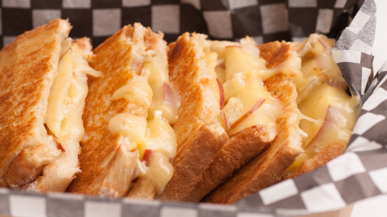 Grilled cheeses with apple slices and brie in a box lined with black-and-white checkered parchment paper