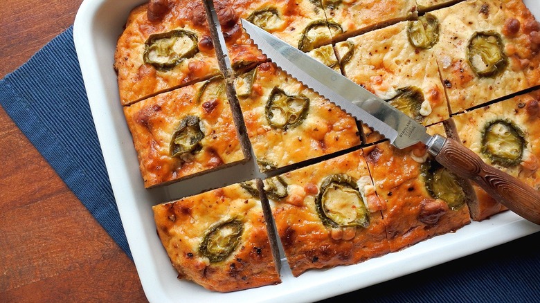 Rectangular pan of cut cornbread topped with jalapeños and a serrated knife