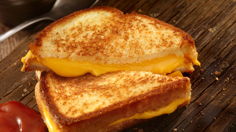 A grilled cheese sandwich on a wooden board with a side of ketchup.