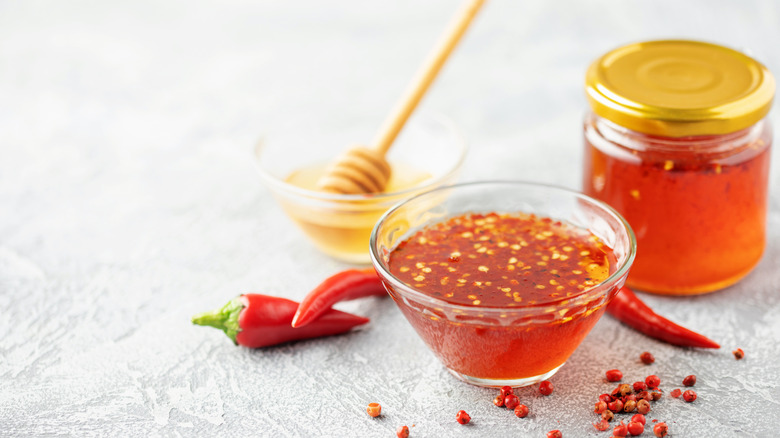 A bowl of hot honey with chili flakes beside whole red chilis.