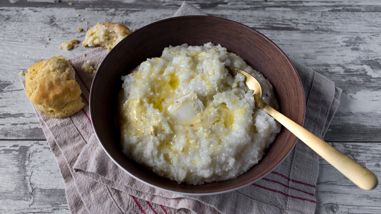 A bowl of buttery grits with a biscuit on the side.