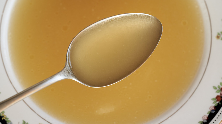A bowl of chicken broth with a metal spoon.
