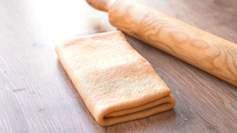 Dough folded into thirds on a wooden surface next to wooden rolling pin