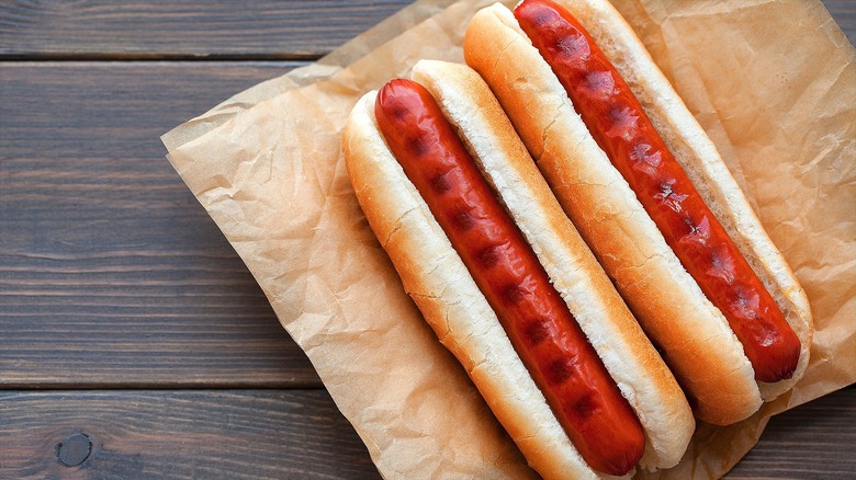 Two grilled hot dogs in buns over two sheets of brown parchment paper